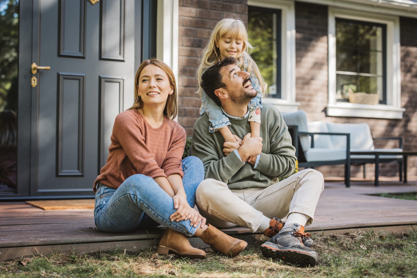 The Beginner's Guide to Marketing Personas for Homebuilders. Young family with little girl having fun in front of there house. Porch is decorated with flowers.